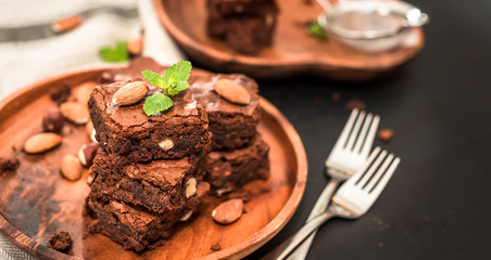 homemade, chocolate brownie with hazelnuts and almonds in a wooden plate on a black background