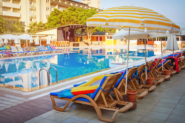 Fototapeta na wymiar Sunbeds and sun umbrellas near pool of tropical resort hotel in summer. Turkey
