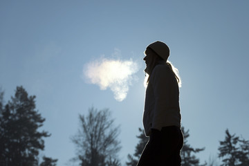 Silhouette of a woman with hat breathing warm air during a cold winter morning. Selective focus...