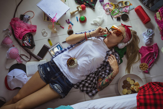 after studying blonde student, lying on the floor in headphones and sunglasses, listening to music and smoking a cigarette. The image of a modern student, education, Accessories of a modern young girl