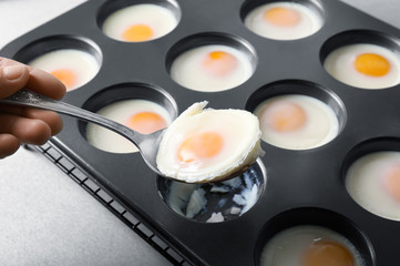Woman holding spoon with baked egg over muffin tin