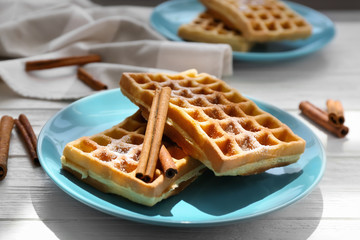 Tasty homemade waffles with sugar powder and cinnamon sticks on plate