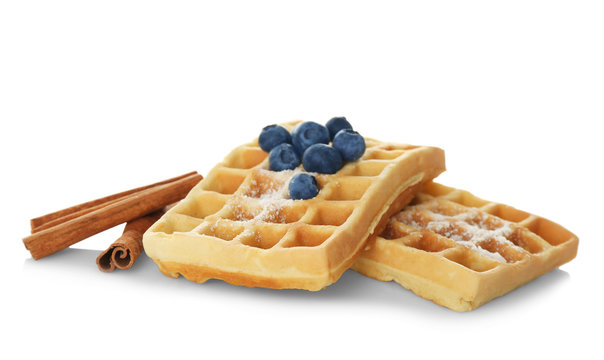 Tasty homemade waffles with sugar powder, cinnamon sticks and blueberries on white background