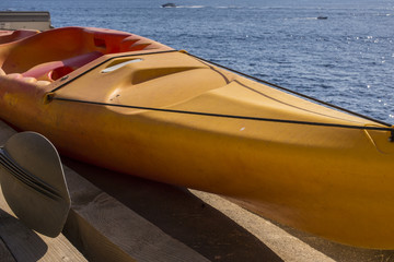 Dettaglio di una canoa gialla monoposto ferma sulla spiaggia. Nel mare gommoni, barche e moto...