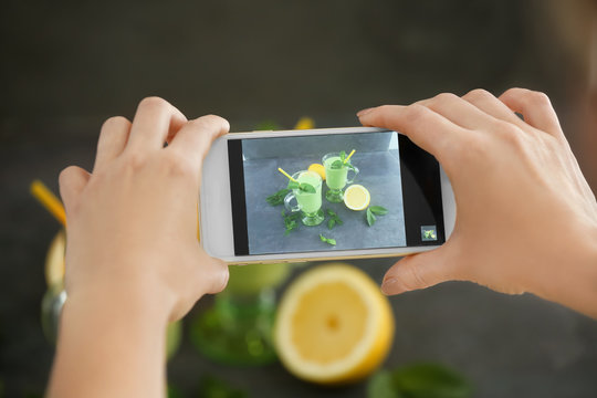 Woman taking photo of smoothies with smart phone in studio. Concept of food photography