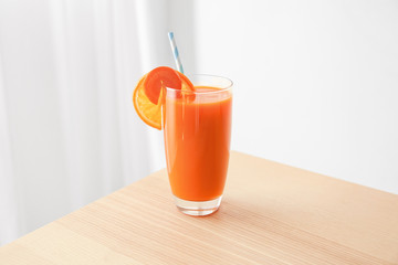Glass with fresh juice, carrot and orange slices on wooden table