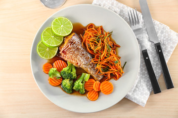 Plate with delicious fish, sauce and vegetables on table