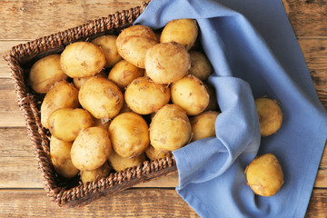 Wicker basket with young potatoes on wooden table