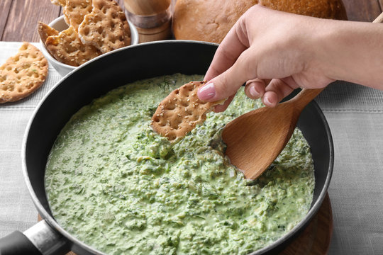 Female hand dipping cookie into frying pan with spinach sauce