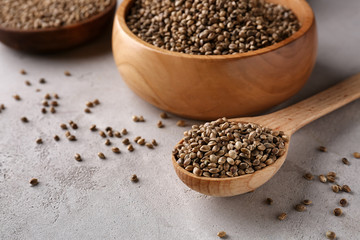 Wooden spoon and bowl with hemp seeds on grey background