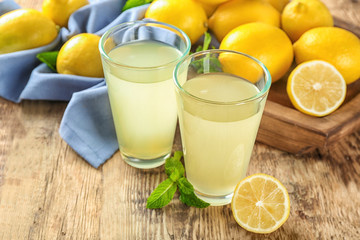 Glasses of lemon juice and fresh lemons on wooden table