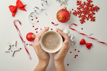 Female hands with cup of coffee and Christmas decorations on light background