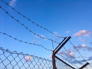 Barbed wire on top of an iron fence against a blue sky