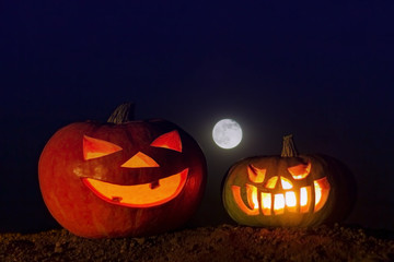 Two glowing pumpkins on the ground and a full moon in the dark blue sky. Picture for decoration on the holiday of Halloween.