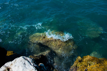 Fototapeta na wymiar turquoise sea waves cracking against colored rocks