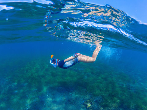 Snorkeling woman dives to sea bottom. Snorkeling girl in full-face snorkeling mask.
