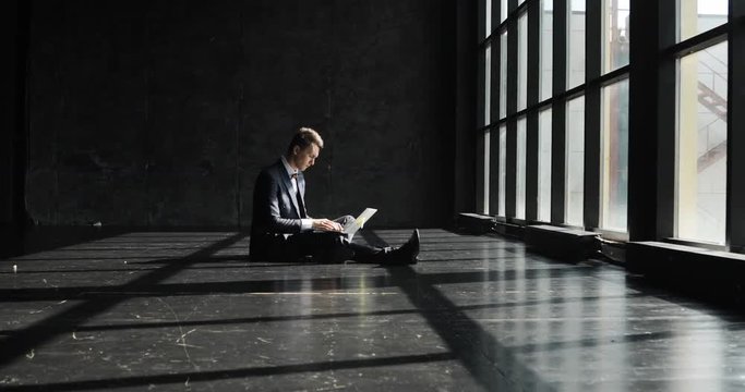 Successful young Man Working In Home Office in loft style. Stylish hipster man in a suit working against a blavk wall background lit by sunlight