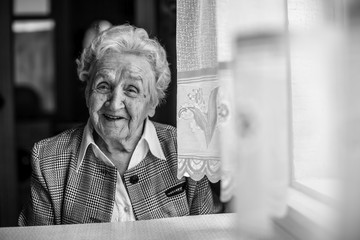 An elderly woman black and white portrait near the window.