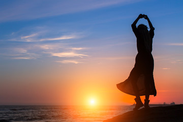 Silhouette of dancing woman on the sea coast during amazing sunset.