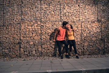 two young adult people, sitting rocks, outdoors nature forest asphalt, sport clothes, kiss hug, walkway