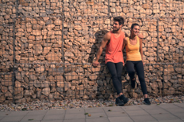 two young adult people, man woman friendship, sitting rocks, outdoors rocks, sport clothes, walkway