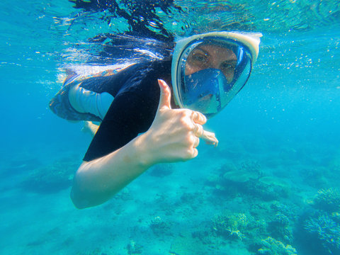 Snorkeling woman shows thumb. Snorkeling girl in full-face snorkeling mask.