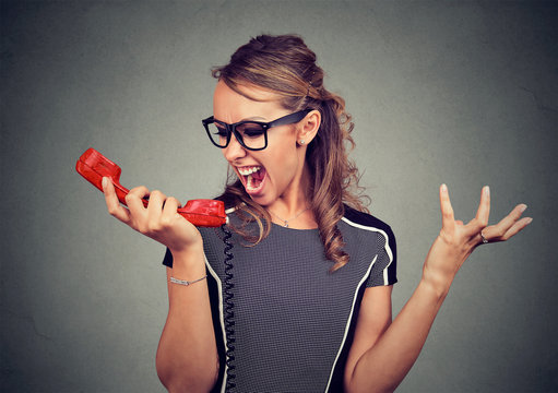 Young angry woman yelling into red phone
