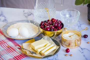Ingredients for the pie - cherry, flour, eggs, sugar, water and butter on a white marble tabletop