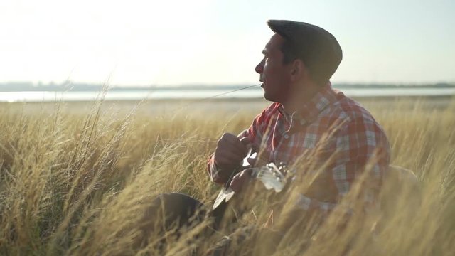 Handsome boy plays ukulele at wheat field sunrise rapid slow motion