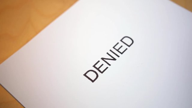 An unidentified person stamps the word DENIED on a stack of blank paper.  	