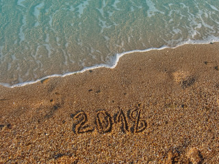 The year 2018 - on the sea sand with aquamarine rolling wave. Sunny vacation day. Natural background with place for text