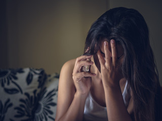 Closeup portrait of sad young woman sitting by sofa with cell phone at home.