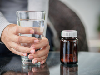Closeup young woman holding drinking water glass in her hand with pills bottle. Health care concept.