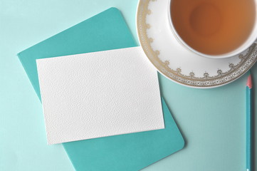 White fine china cup of tea with a blank note card and teal book on mint background
