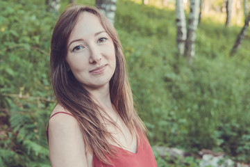 Fototapeta premium Young woman portrait in a summer forest in the mountains. Pretty girl in red dress in summertime