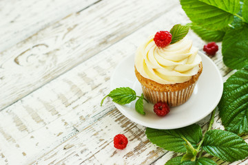 Delicate vanilla cupcakes with cream and raspberries on a white wooden background