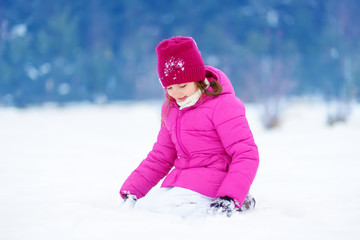 Fototapeta na wymiar Adorable little girl having fun in beautiful winter park. Cute child playing in a snow.