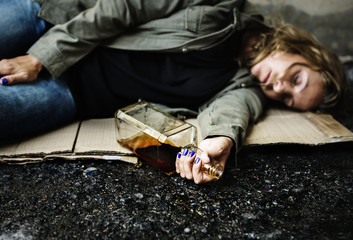 Homeless woman lay down on the ground holding alcohol