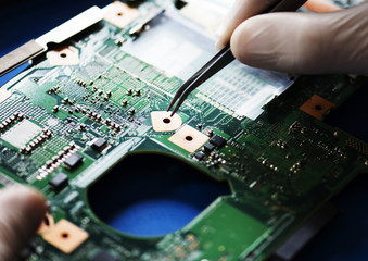 Closeup of hands with computer motherboard and tweezers