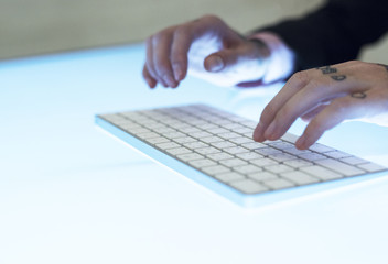 Hands with tattoo typing on a keyboard