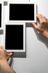 Woman hands holding and adjusting white photo frames mockup hanging on white wall