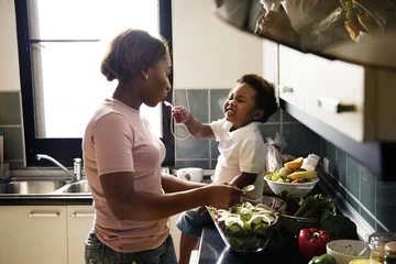 Wall murals Cooking Black kid feeding mother with cooking food in the kitchen