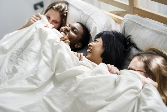 Group of diverse women lying on bed together covered with blanket