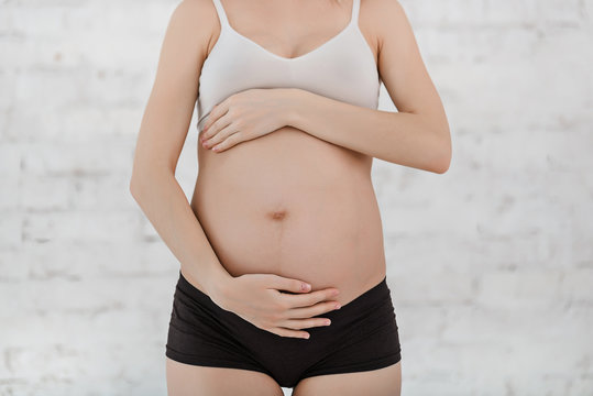 Pregnant belly on white background. Hands, stomach, shirt and t-shorts