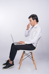 Smart casual asian man seated on chair, using laptop in studio background