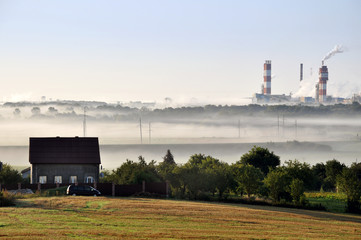 Pipes of working Nitrogen plant in smoke in summer morning.  Abandoned village in the foreground. Grodno, Belarus.