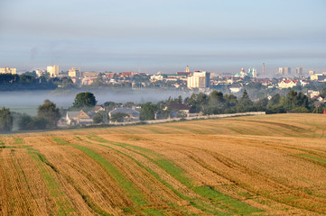 Agricultural field after harvest in the foreground. Morning city covered with fog in the background. Grodno, Belarus.