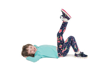 A little girl in sports clothes is lying on the floor and is engaged in gymnastics. White isolated background.