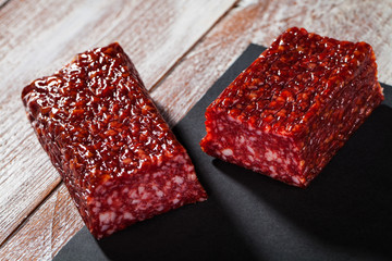 dry sausage is cut by pieces with seasonings on a wooden background