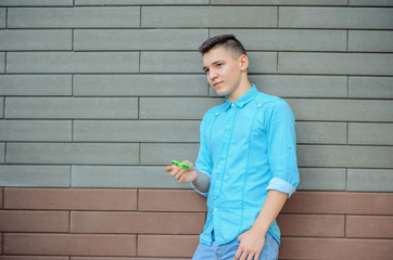 Pensive young man on the azure shirt  and blue jeans hand holding popular gadget fidget spinner